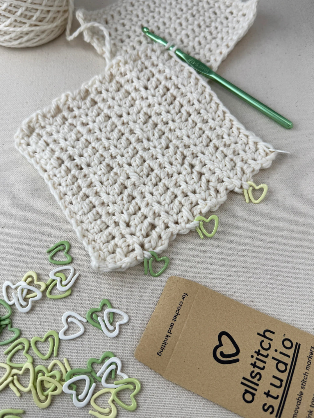 Green and white heart shaped stitch markers shown with a sample