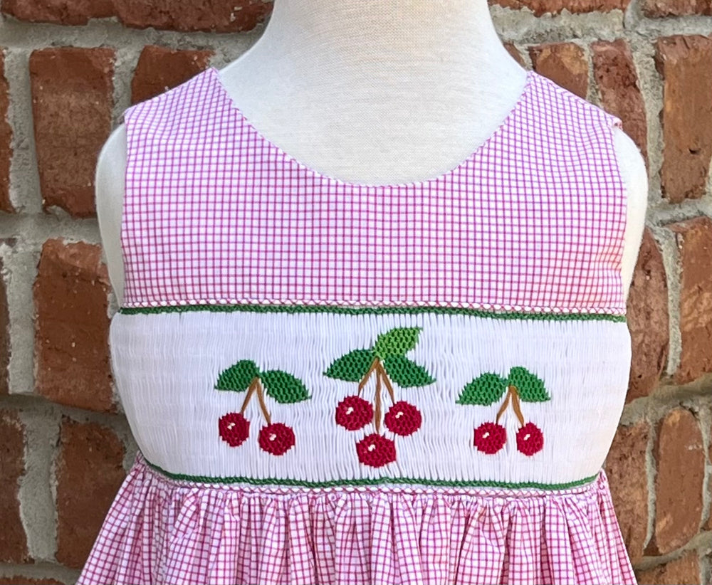 Mannequin wearing a pink checkered dress with cherry design against a brick wall.