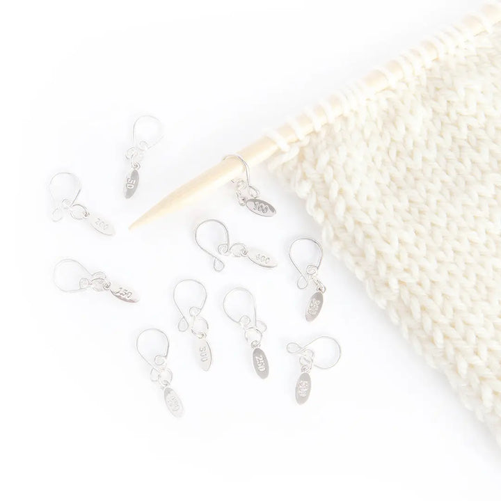 a swatch of cream colored stockinette active on a wooden knitting needle, with some metal stitch markers on and around the needle