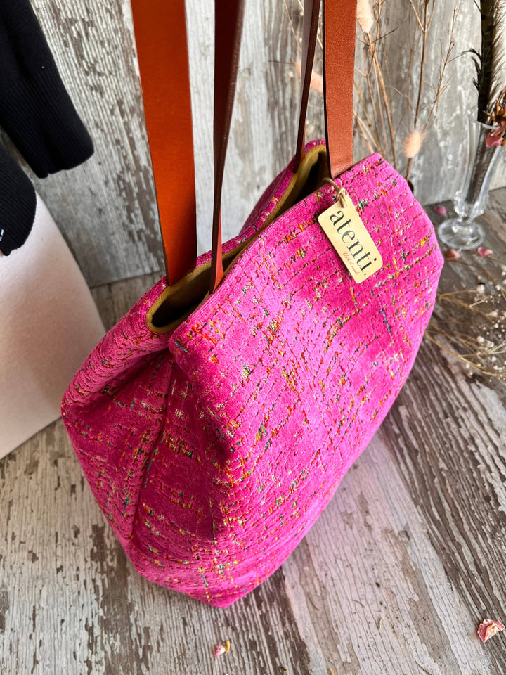 A bright pink woven tote bag with brown leather shoulder straps and a small beige brand tag reading 'aleniia', photographed on a rustic weathered wood surface.