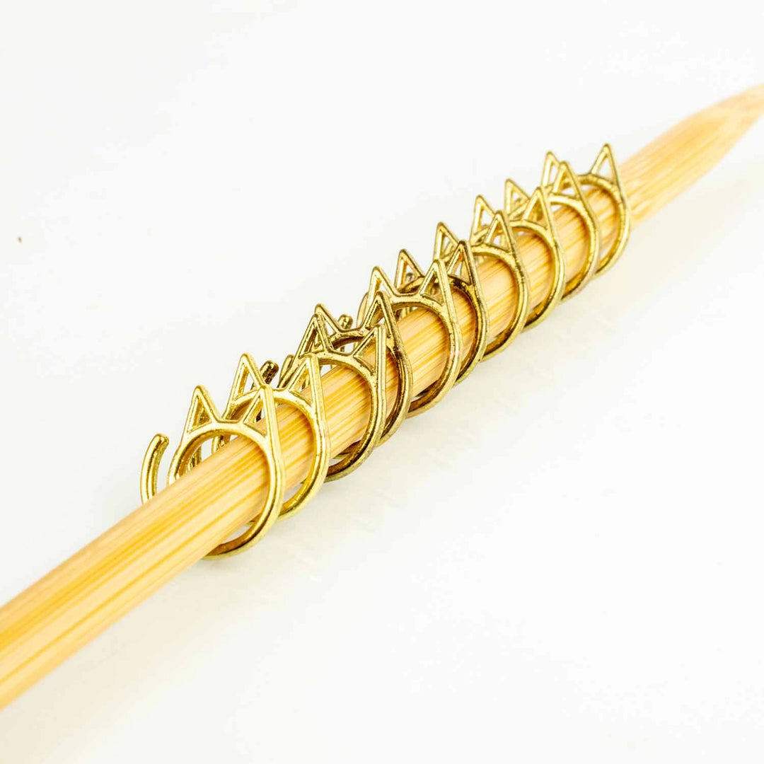 Gold cat shaped stitch markers on a knitting needle.