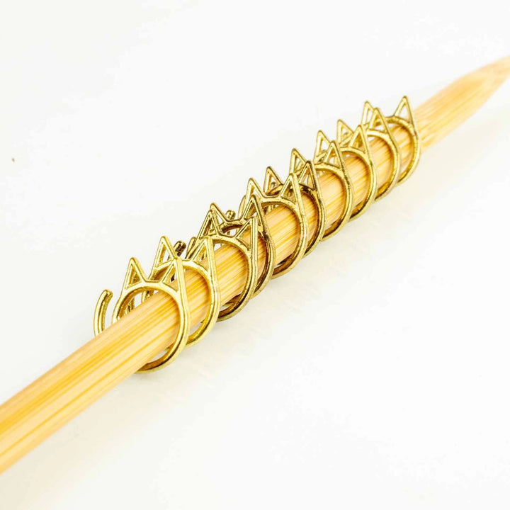 Gold cat shaped stitch markers on a knitting needle.