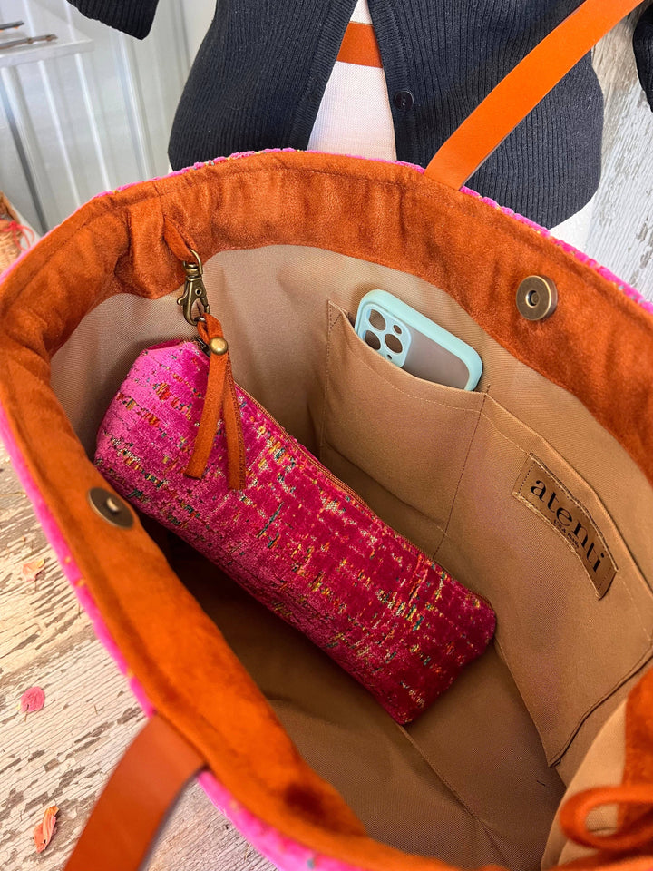An orange and pink tote bag shown open, revealing a beige interior with a phone pocket and a pink patterned pouch inside. A brand label reading 'ALEXANDER' is visible on the bag's interior.