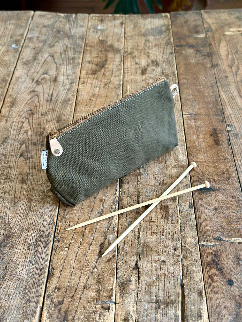 Green zippered pouch with wooden knitting needles on a wooden surface