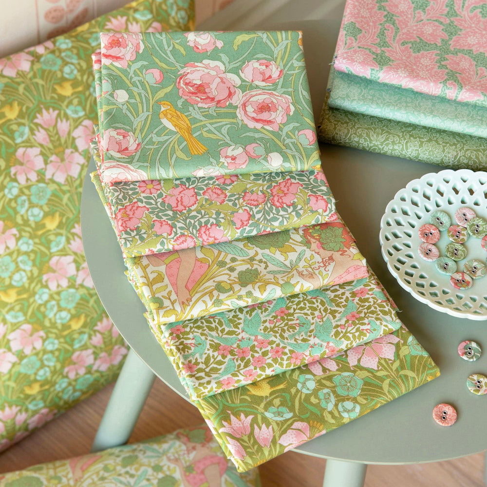 Stack of floral fabric samples on a table with a chair and decorative items.