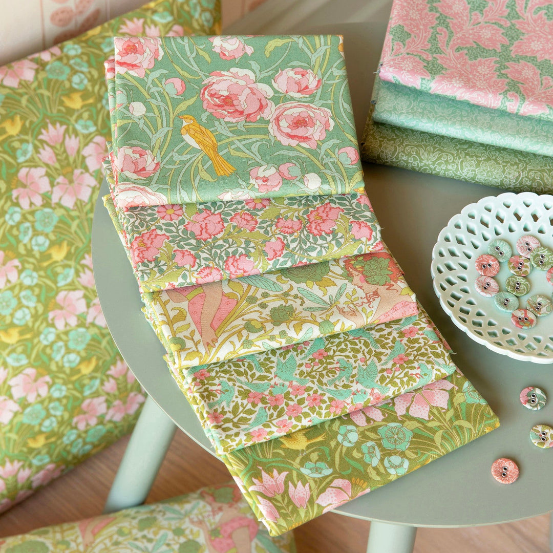 Stack of floral fabric samples on a table with a chair and decorative items.