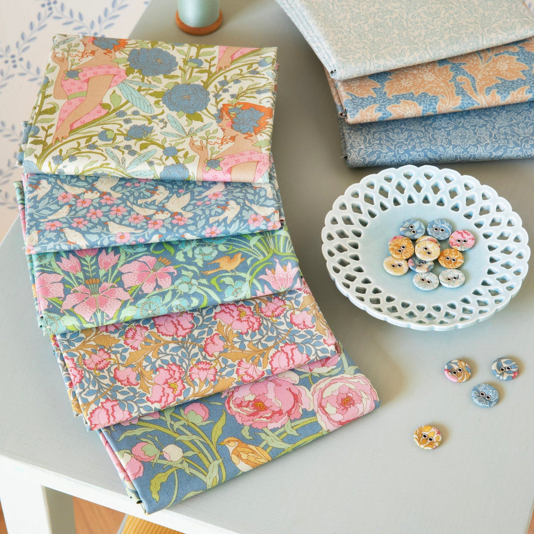Collection of floral fabric swatches on a table with a bowl of buttons.