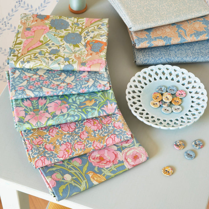 Collection of floral fabric swatches on a table with a bowl of buttons.