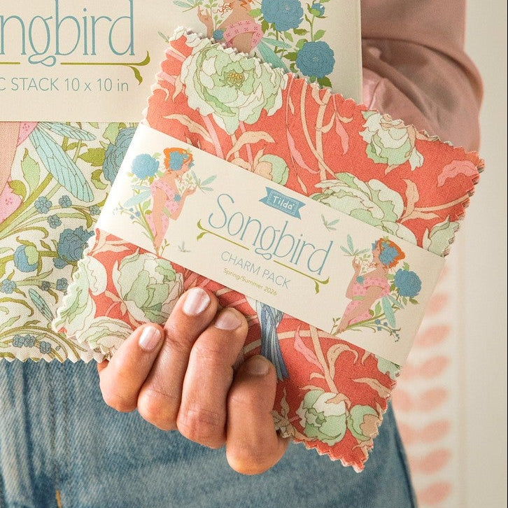 Person holding two floral fabric stacks with 'Songbird' branding.