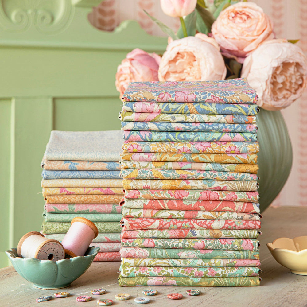 Stack of colorful fabric rolls with a vase of flowers on a wooden surface.