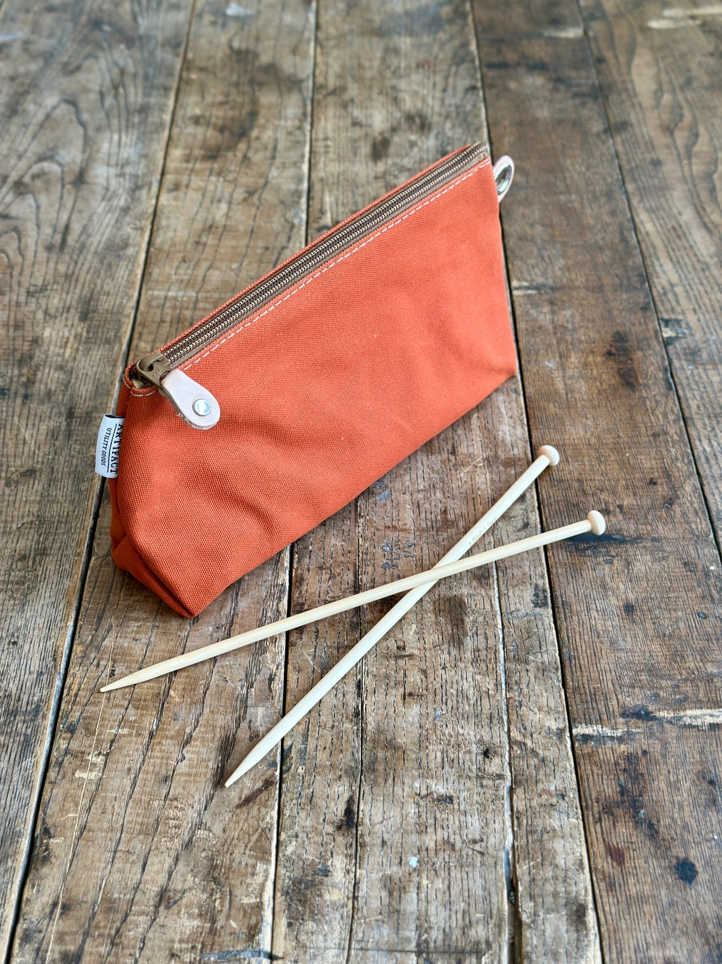 Orange pouch with a zipper and knitting needles on a wooden surface