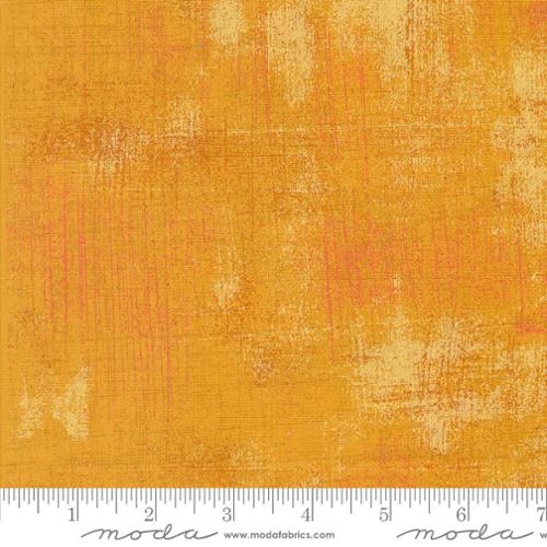 Textured orange fabric swatch with a ruler at the bottom for scale, featuring the Moda Fabrics logo.