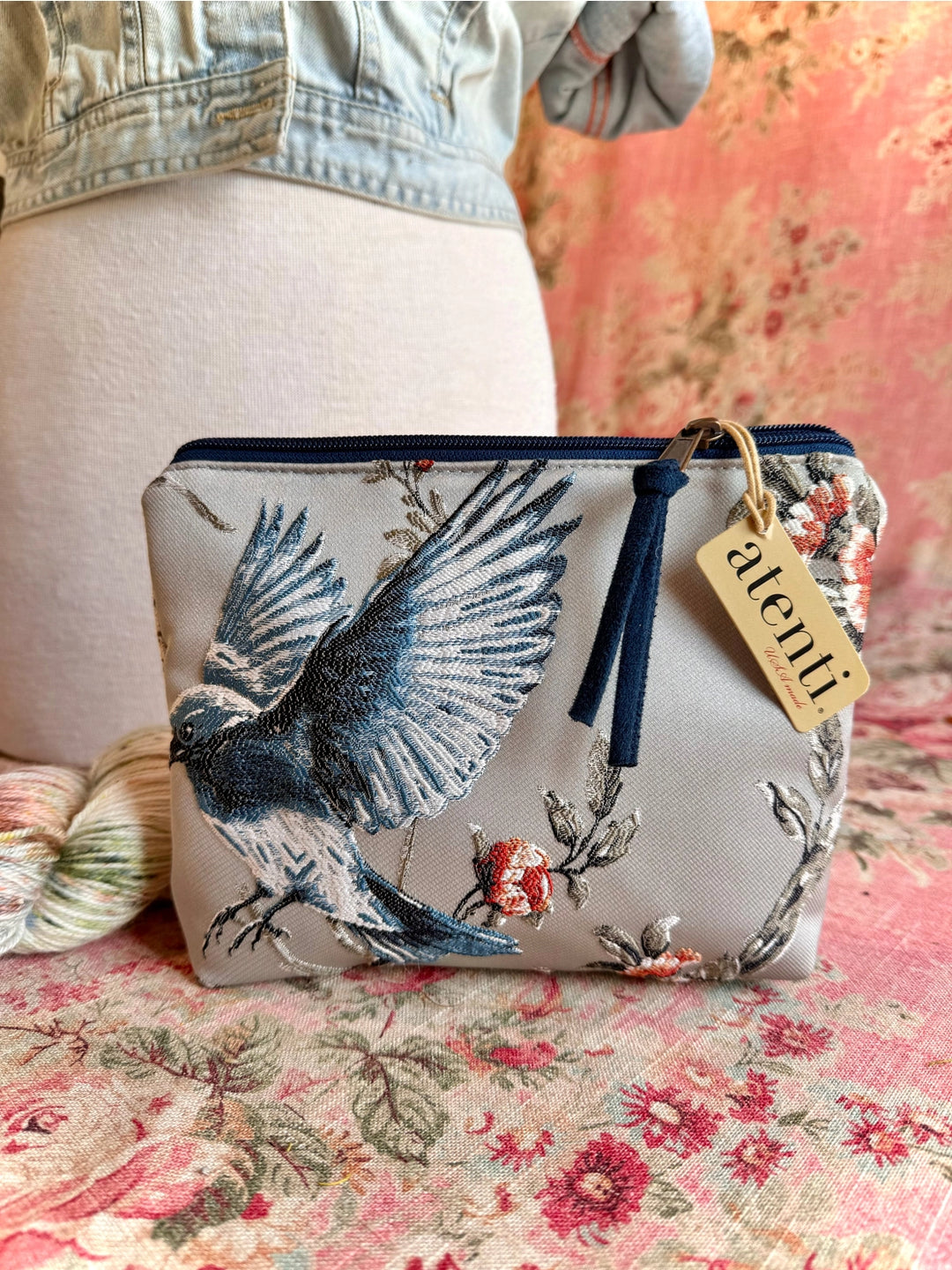 Floral pouch with bird design on a floral surface, featuring a brand tag.