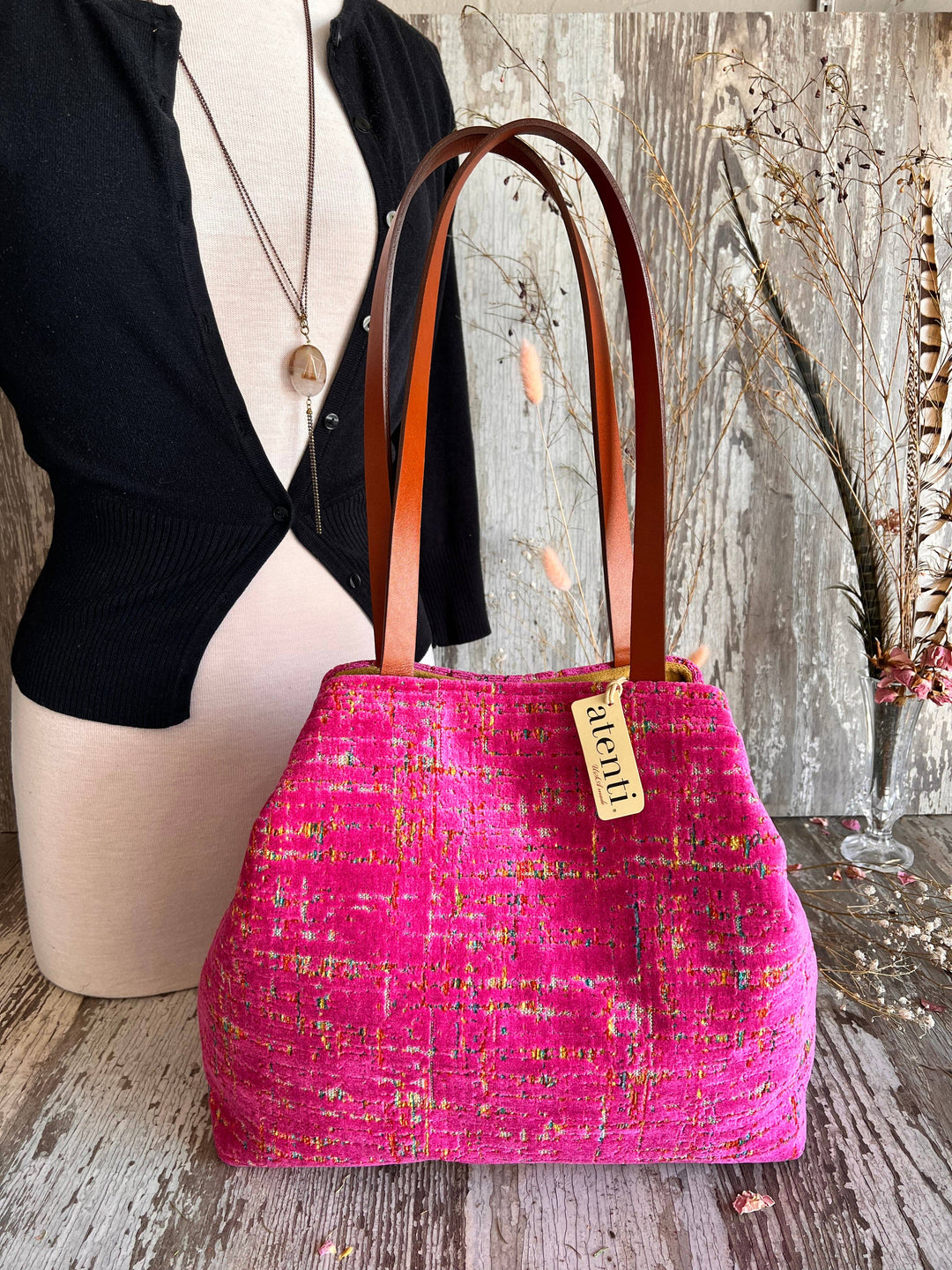 A bright pink tweed handbag with brown leather shoulder straps and a gold-tone 'Guerlain' tag, displayed on a rustic wooden surface next to a mannequin torso.
