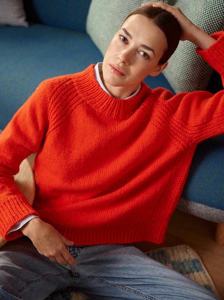 Person wearing a bright red sweater sitting on a couch.