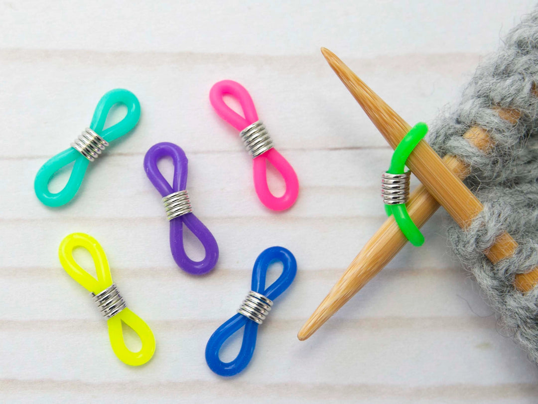 Colorful knitting stitch markers on a wooden surface with a knitting needle and yarn.