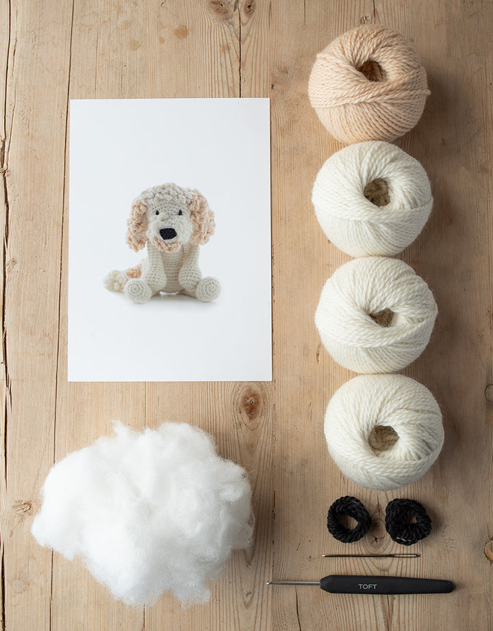 animal card, poly stuffing, balls of yarn, darning needle, and a crochet hook lying on a wooden table