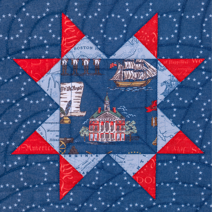 Quilt block with red and blue triangles and a central scene of a building and ship on a blue background.