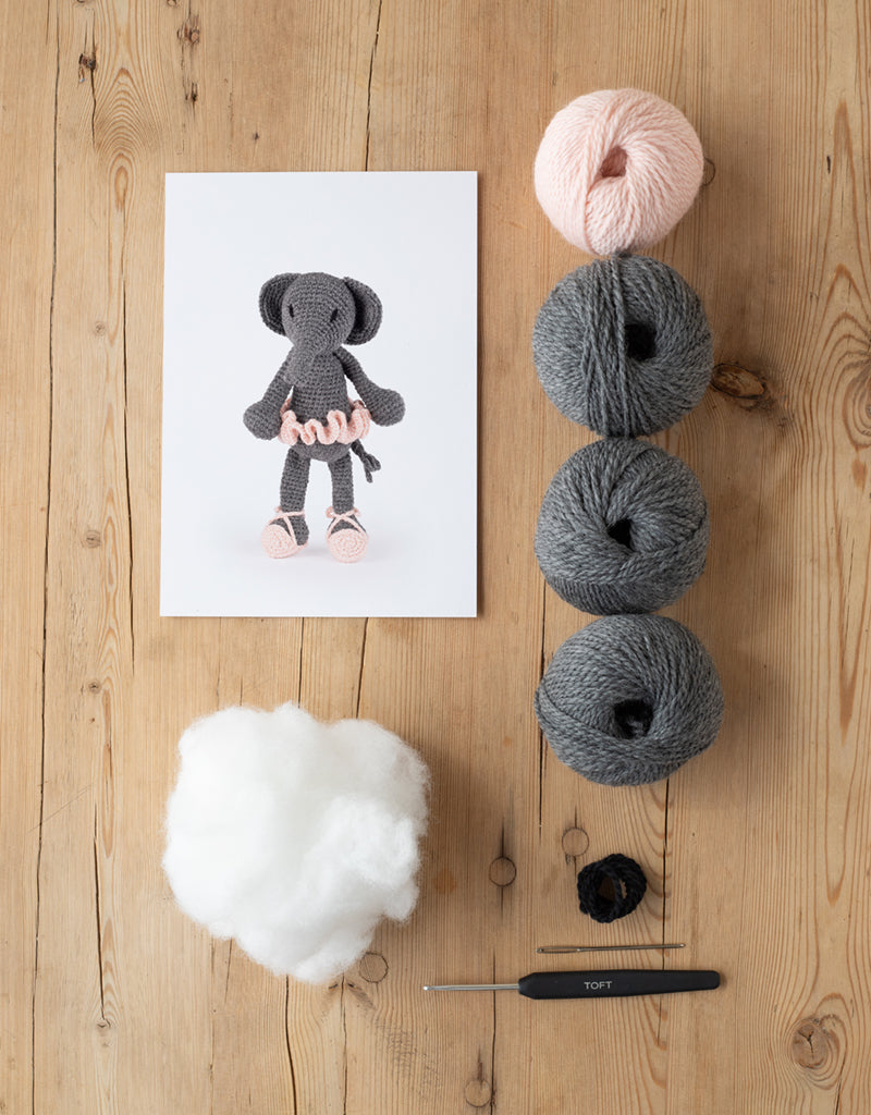 animal card, poly stuffing, balls of yarn, darning needle, and a crochet hook lying on a wooden table