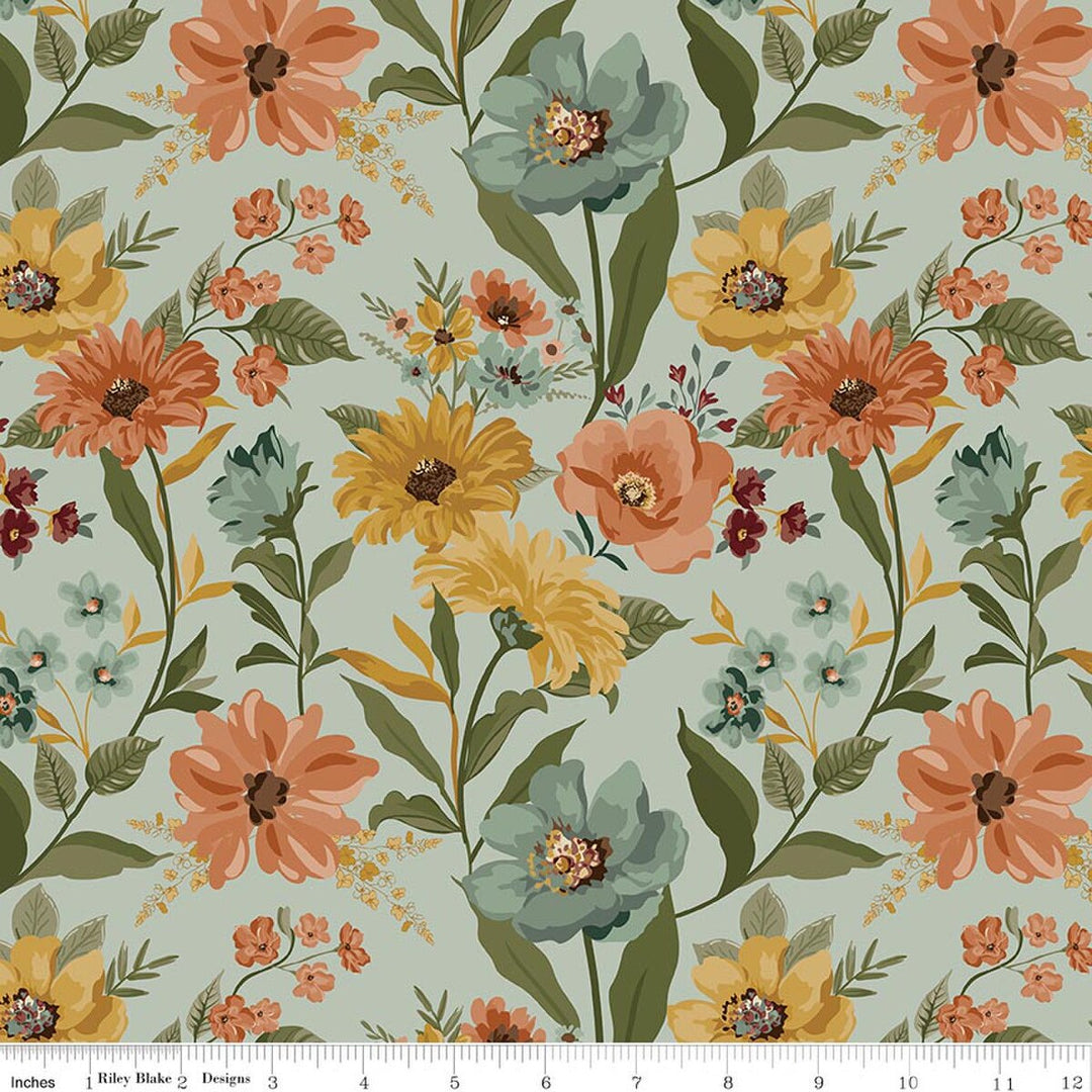 A repeating floral pattern on a light green background with large orange, yellow, and teal flowers, green leaves, and small blossoms. A white ruler strip appears along the bottom edge showing scale.
