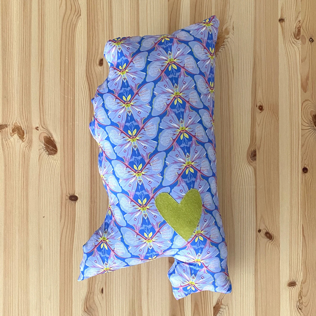 Decorative pillow with butterfly pattern and green heart on a wooden surface