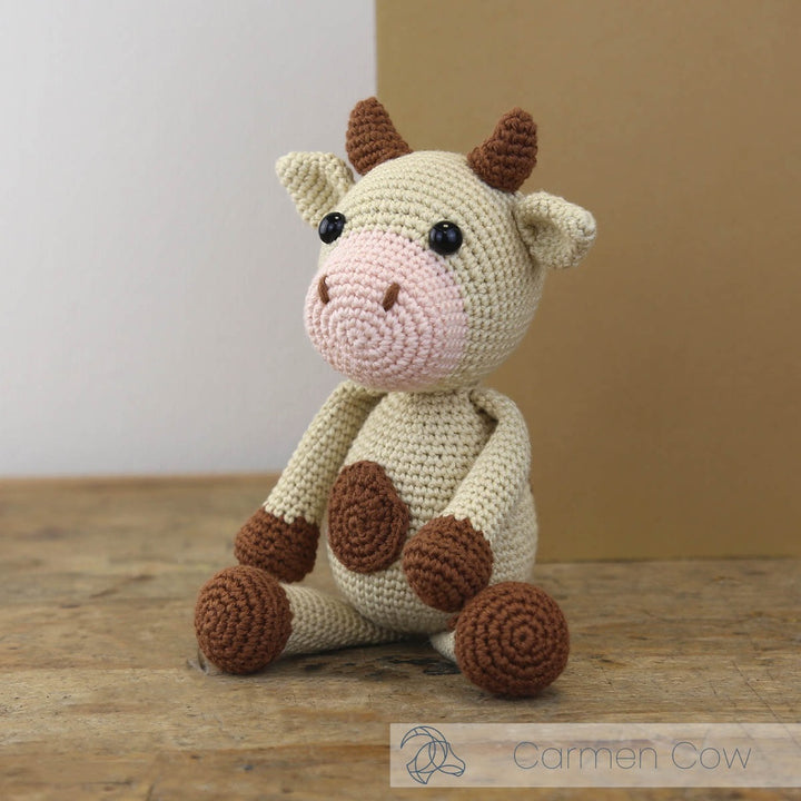 Crocheted cow toy on a wooden surface with a neutral background