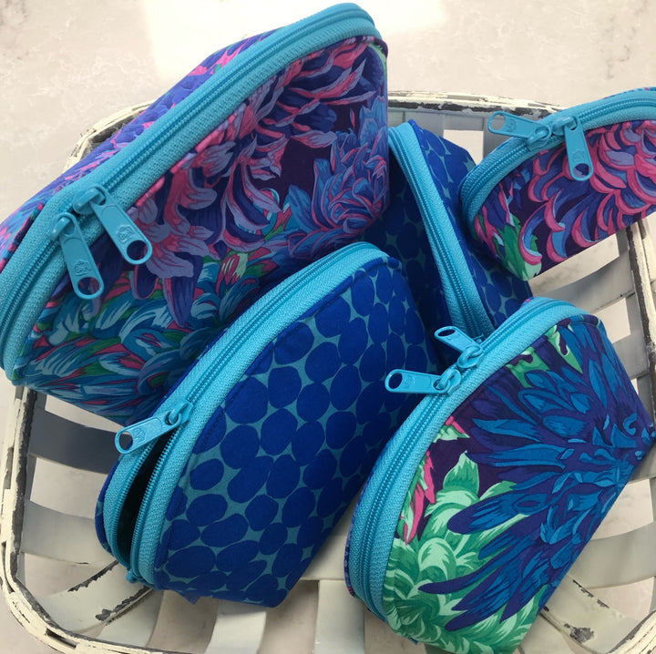 A collection of handmade zipper pouches with floral and geometric patterns, displayed on a metal rack.