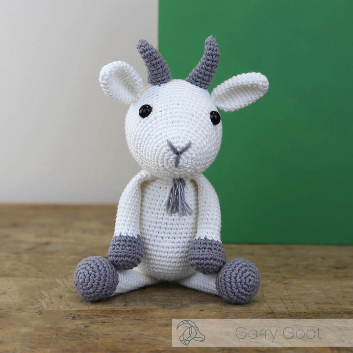 Crocheted goat toy with white body and purple accents on a wooden surface.