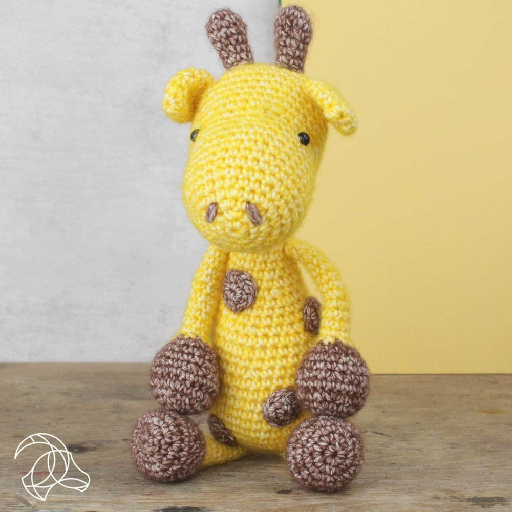 Crocheted giraffe toy with yellow body and brown spots on a wooden surface.