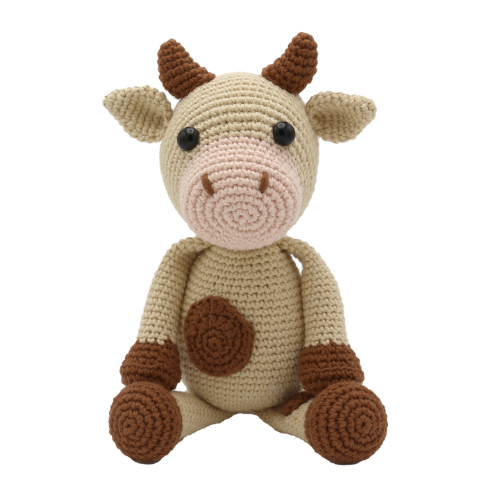 Crocheted toy cow with brown accents on a white background