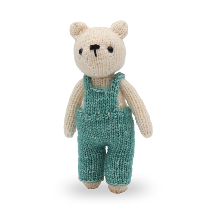 Knitted toy bear wearing teal overalls on a white background