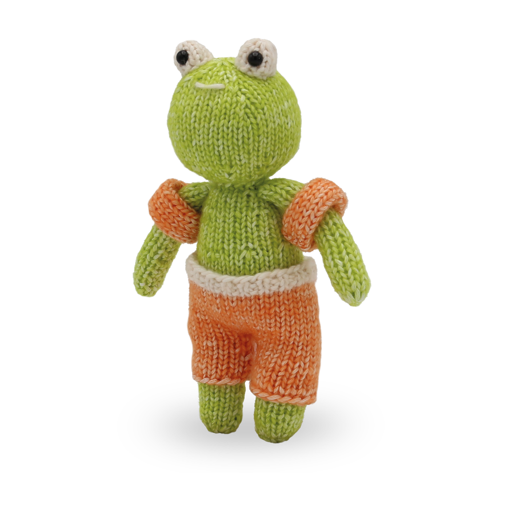 Knitted frog toy with orange shorts on a white background