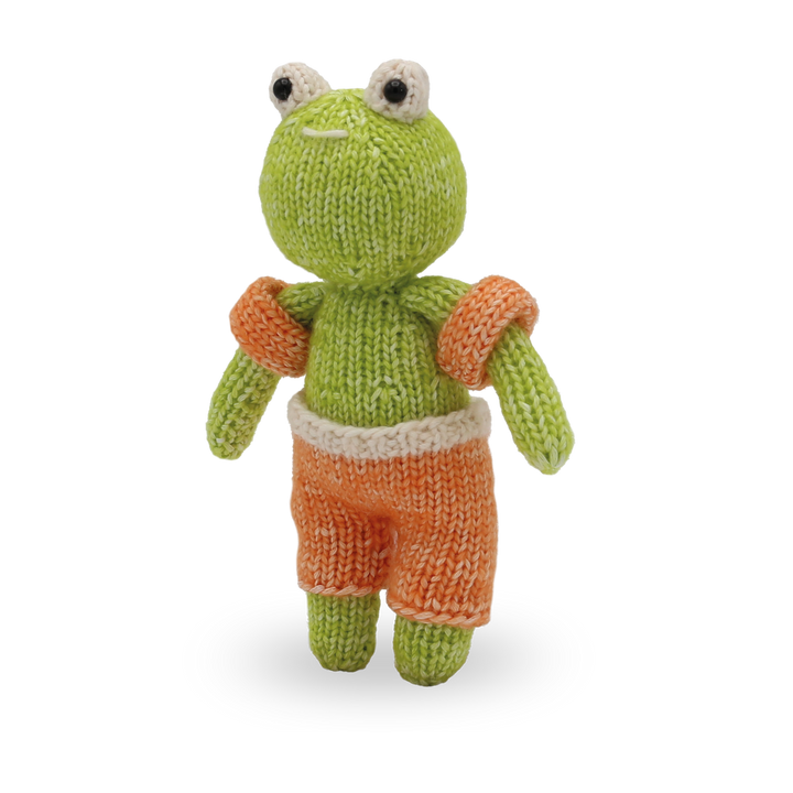Knitted frog toy with orange shorts on a white background