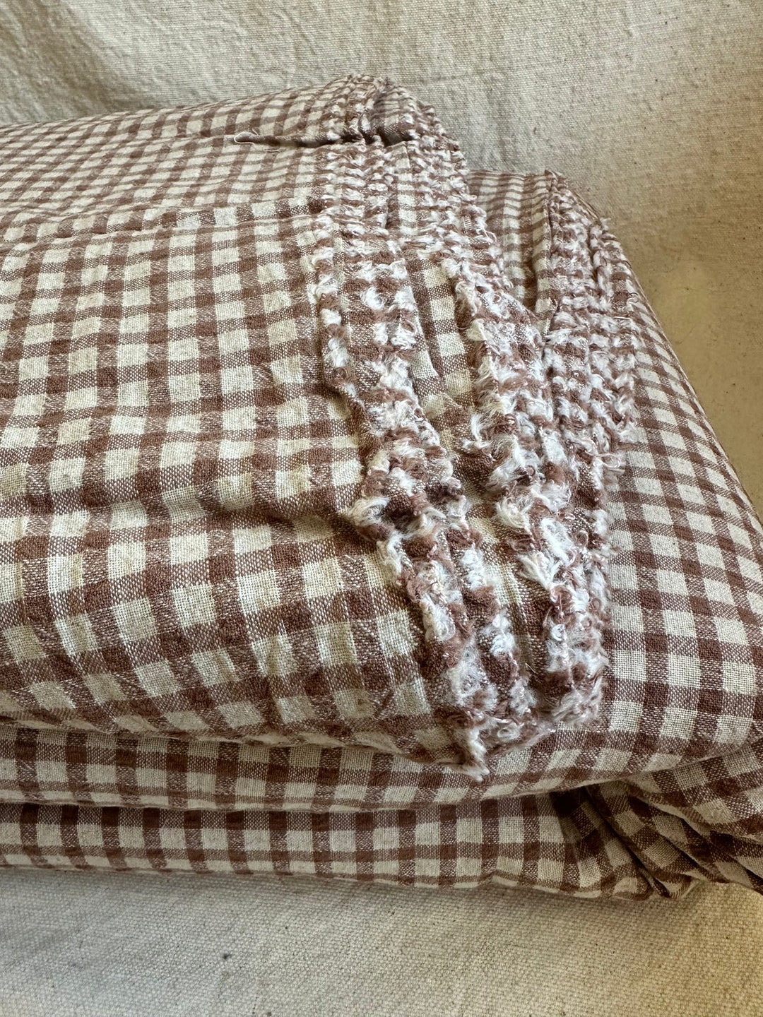 Folded brown gingham fabric resting on linen background. 