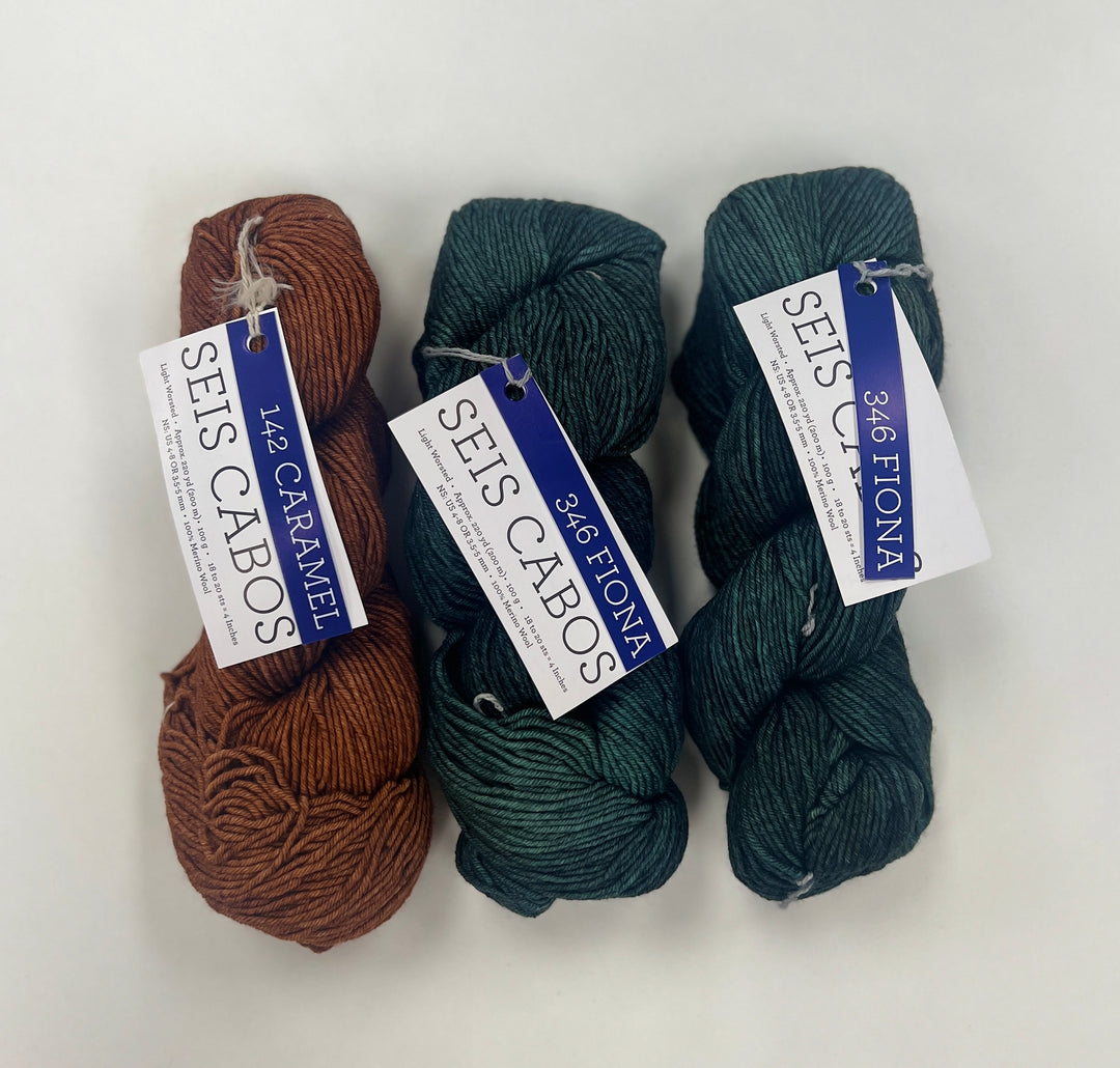 Three skeins of yarn in brown and green/blue with labels on a white background