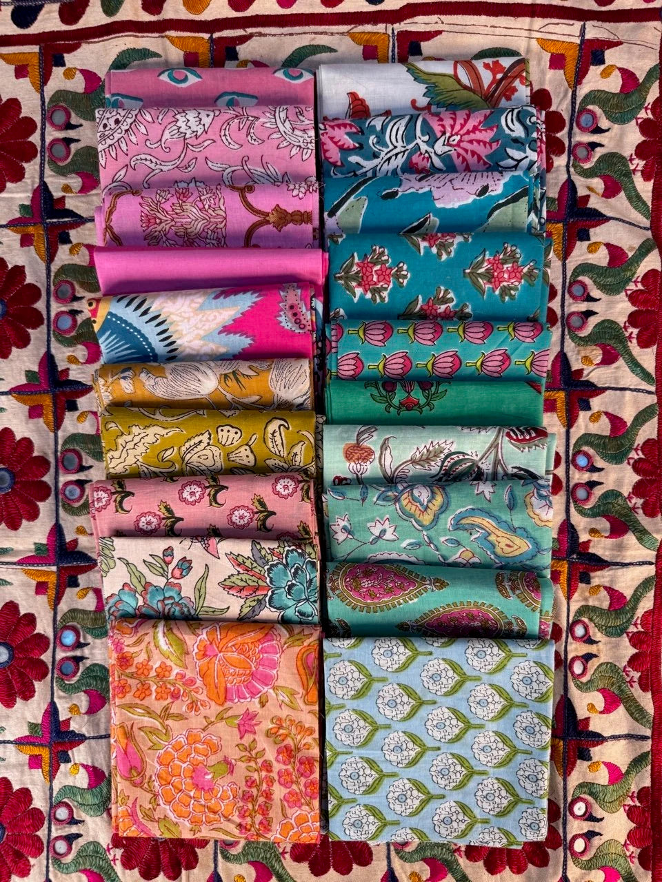 Collection of colorful fabric rolls arranged in a grid on a patterned fabric background.