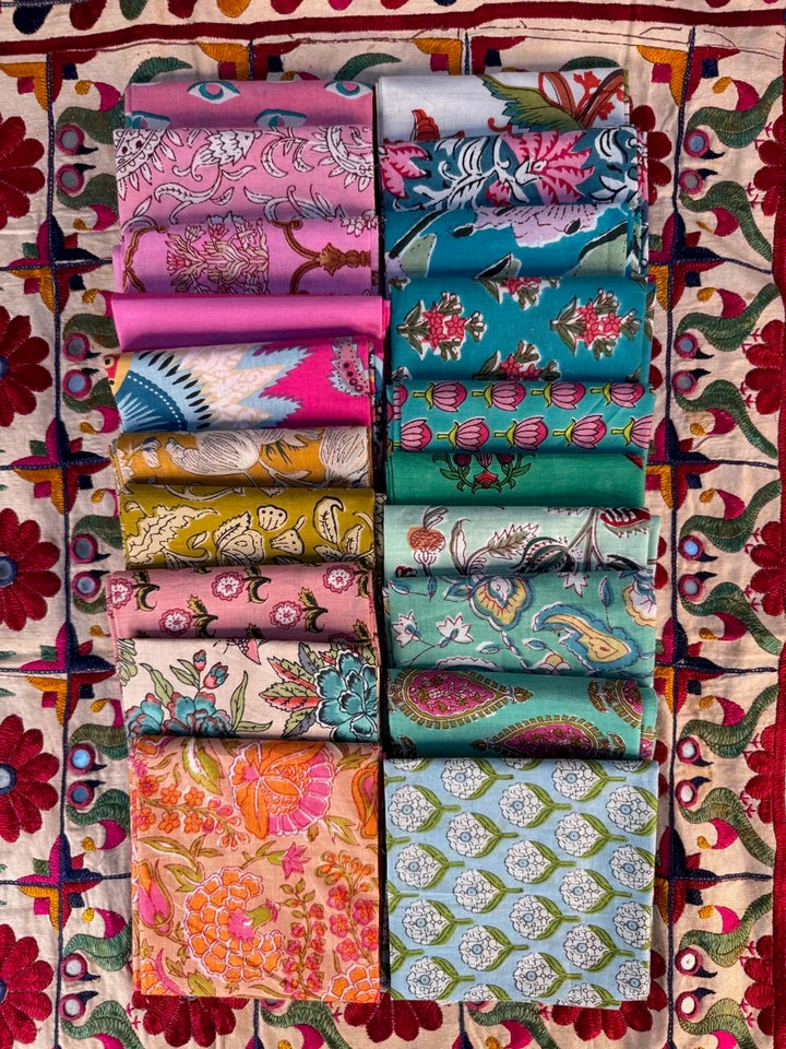 Collection of colorful fabric rolls arranged in a grid on a patterned fabric background.