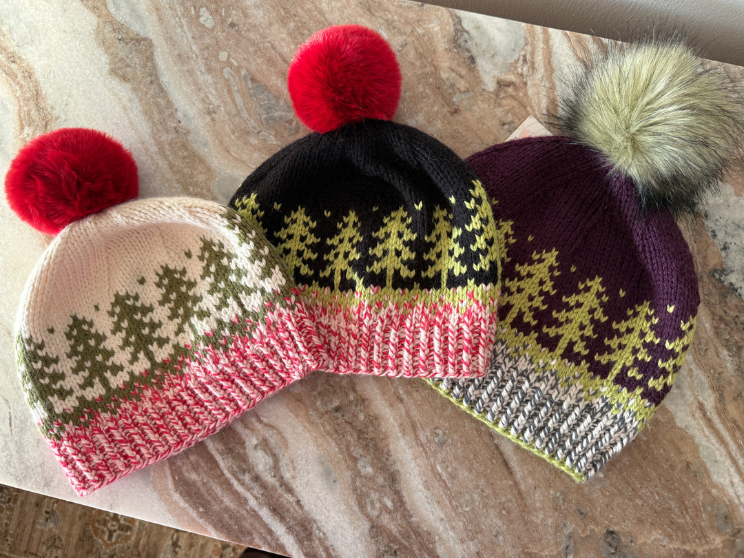 Three knitted hats with pom-poms on a marble surface