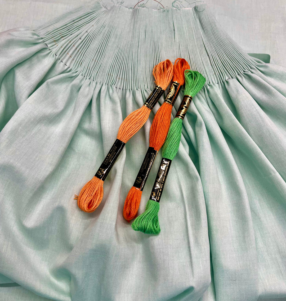 Aqua pleated bishop with two orange and one green embroidery floss