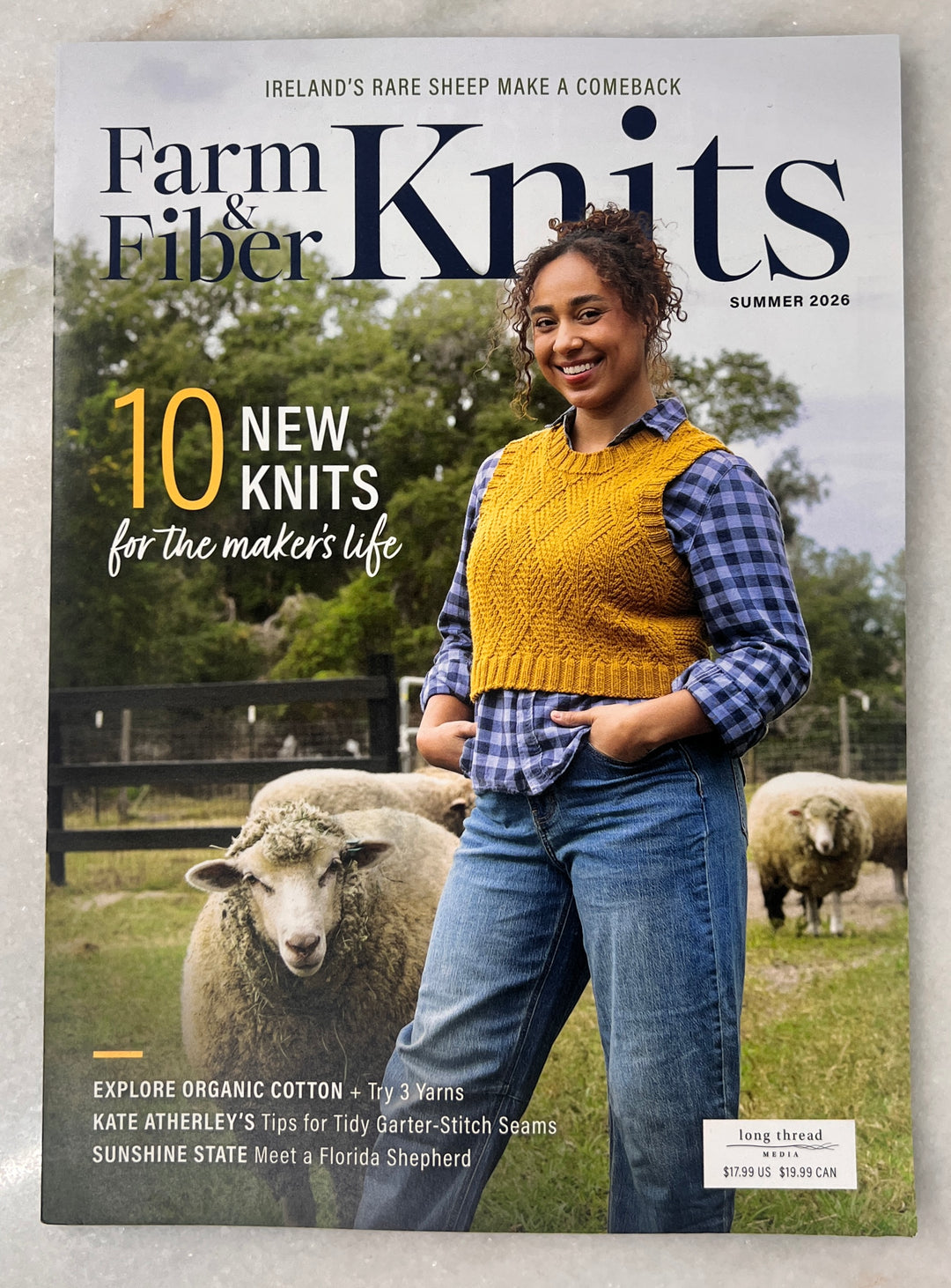 Magazine cover featuring a woman wearing a yellow knit vest with sheep in the background