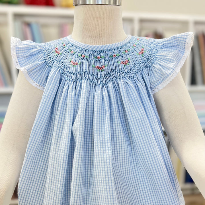 Blue checkered dress with embroidered details on a mannequin against a blurred bookshelf background
