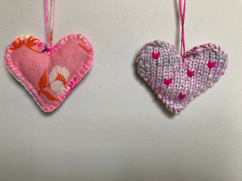 Two heart-shaped decorations, one fabric and one knitted, on a plain background