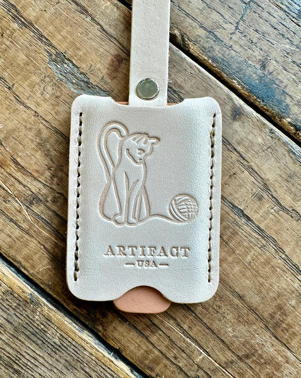 Leather keychain with 'Artifact USA' branding on a wooden surface