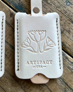 Two white leather luggage tags with embossed designs on a wooden surface