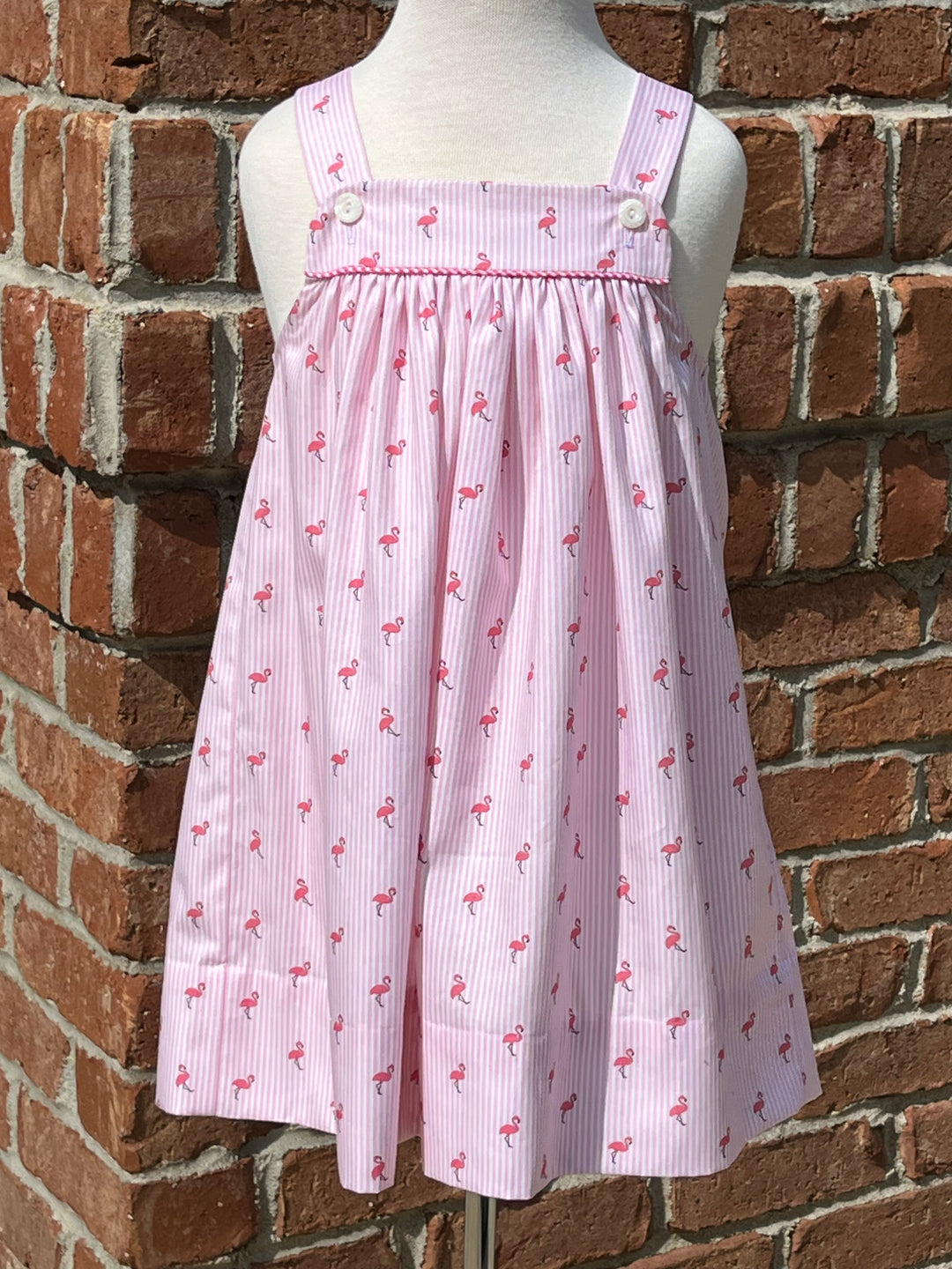 pink striped dress covered in tiny flamingos on a dress form in front of a brick wall