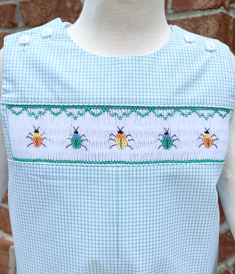 Checkered romper with embroidered beetles on a mannequin against a brick wall.