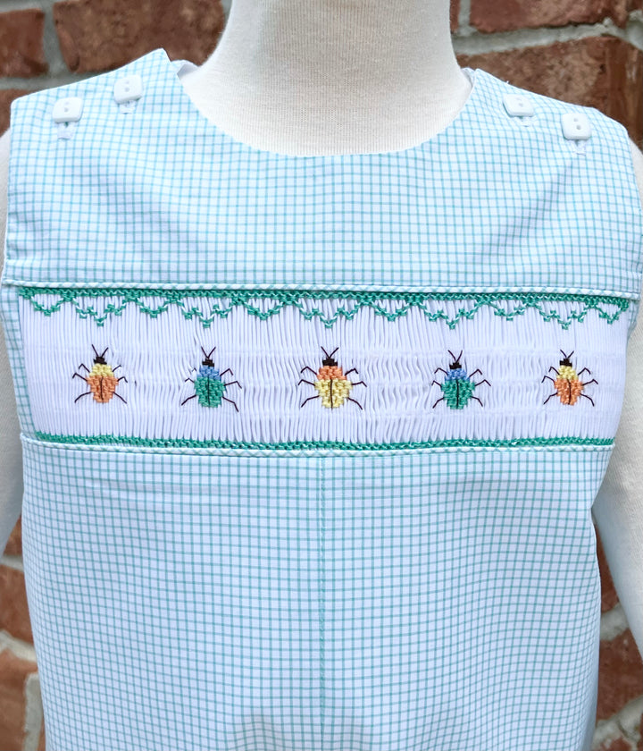 Checkered romper with embroidered beetles on a mannequin against a brick wall.