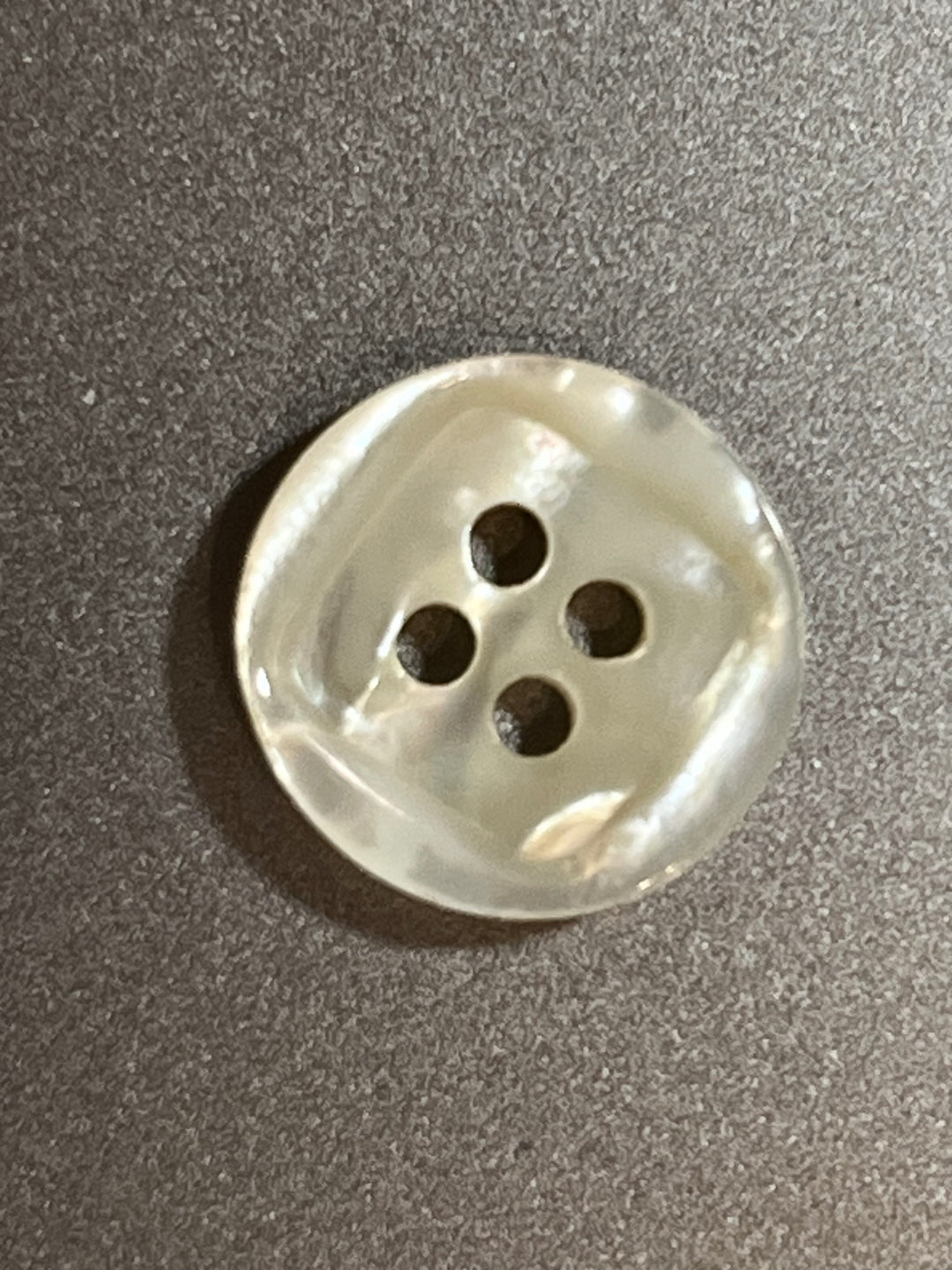 Pearl button with four holes on a gray background
