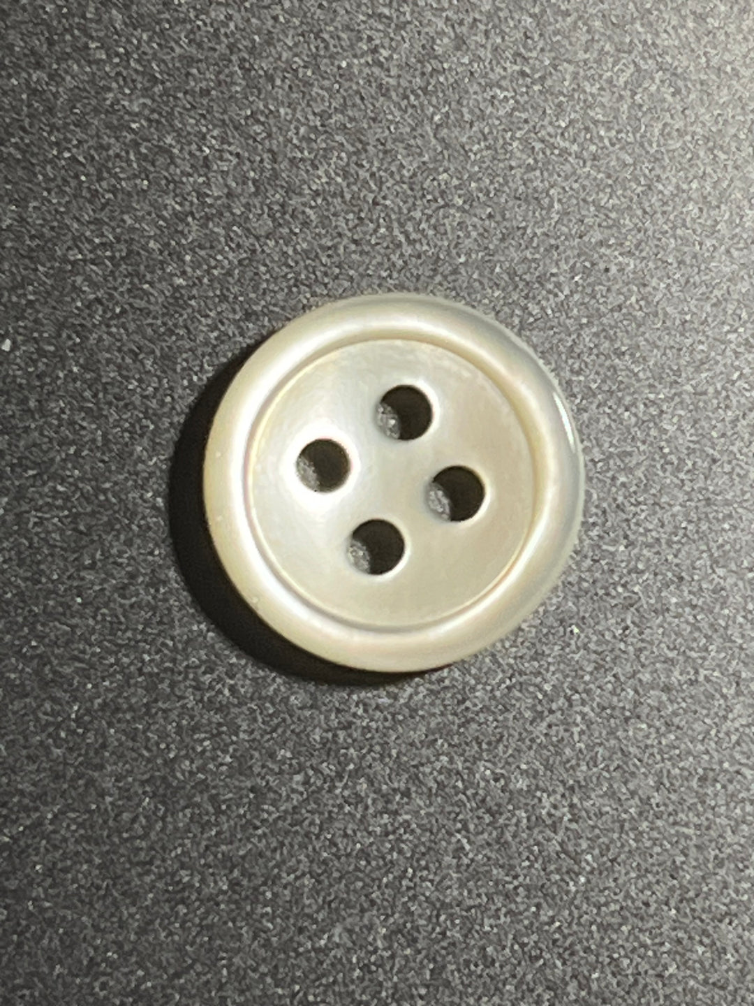 Beige button with four holes on a gray textured background