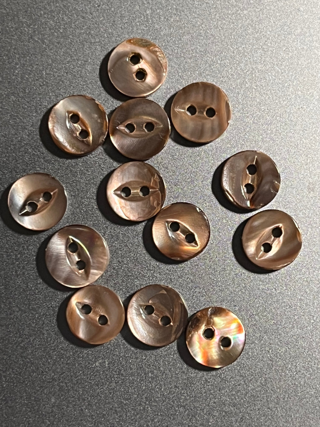 Bronze buttons arranged in a scattered pattern on a gray surface
